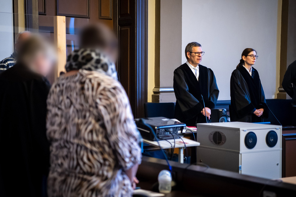 Volker Stronczyk (2.v.r), Vorsitzender Richter, steht vor Prozessbeginn im Gerichtssaal, die Angeklagte (2.v.l) steht neben ihrer Anwältin (l)