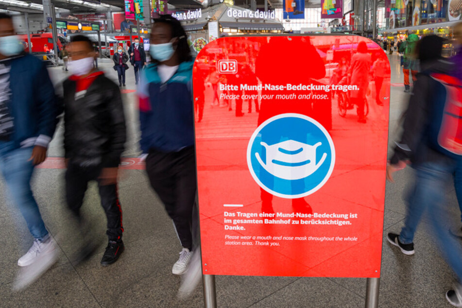 "Bitte Mund-Nase-Bedeckung tragen" steht in deutscher und englischer Sprache auf einem roten Schild im Eingangsbereich des Münchner Hauptbahnhofs.