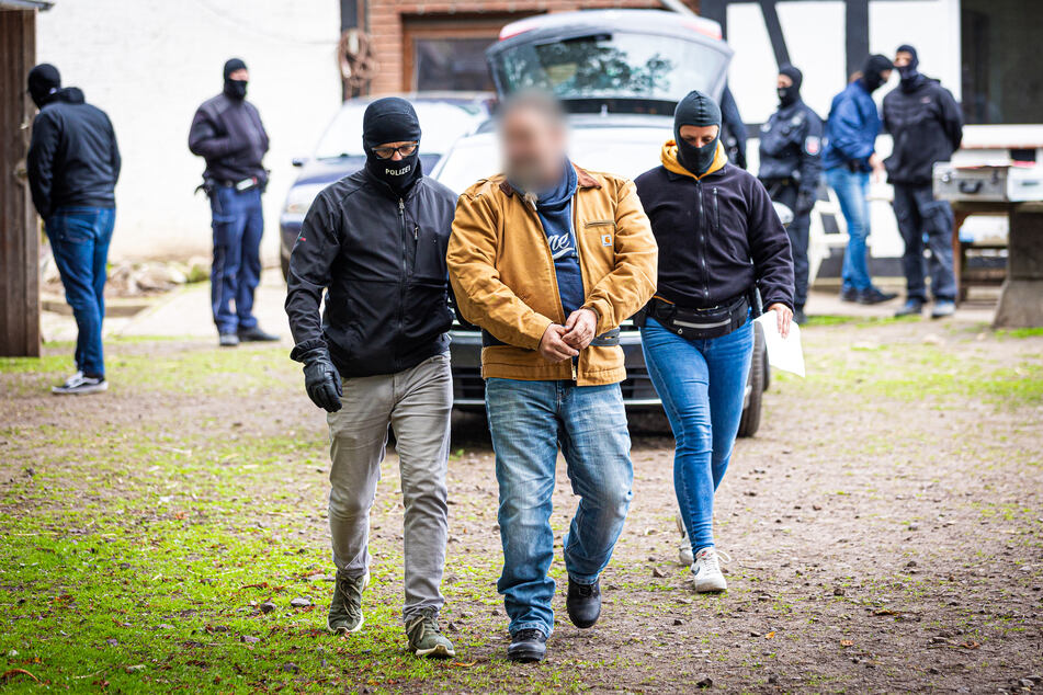 Einsatzkräfte der Polizei führen während einer Razzia auf einem Hof bei Espelkamp einen Mann ab.