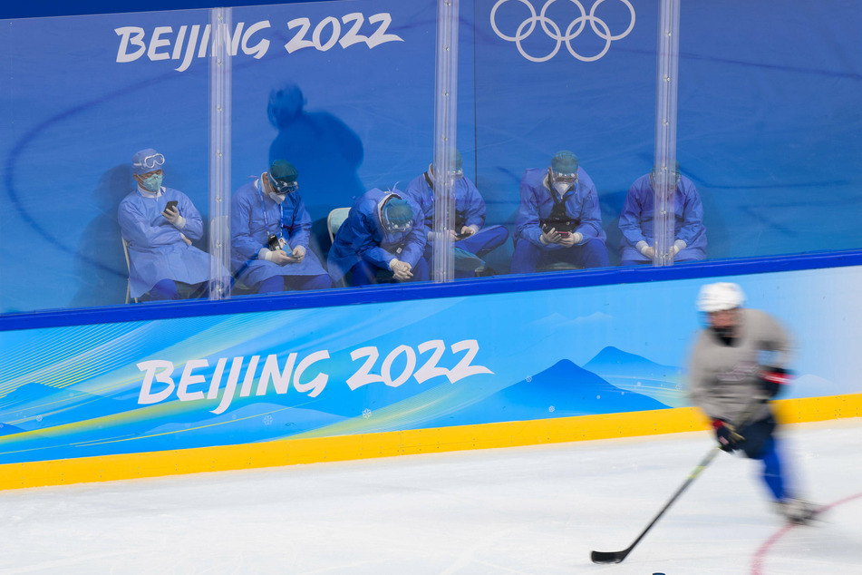 Medical personnel in personal protective gear watch the US women's ice hockey team during their practice session.