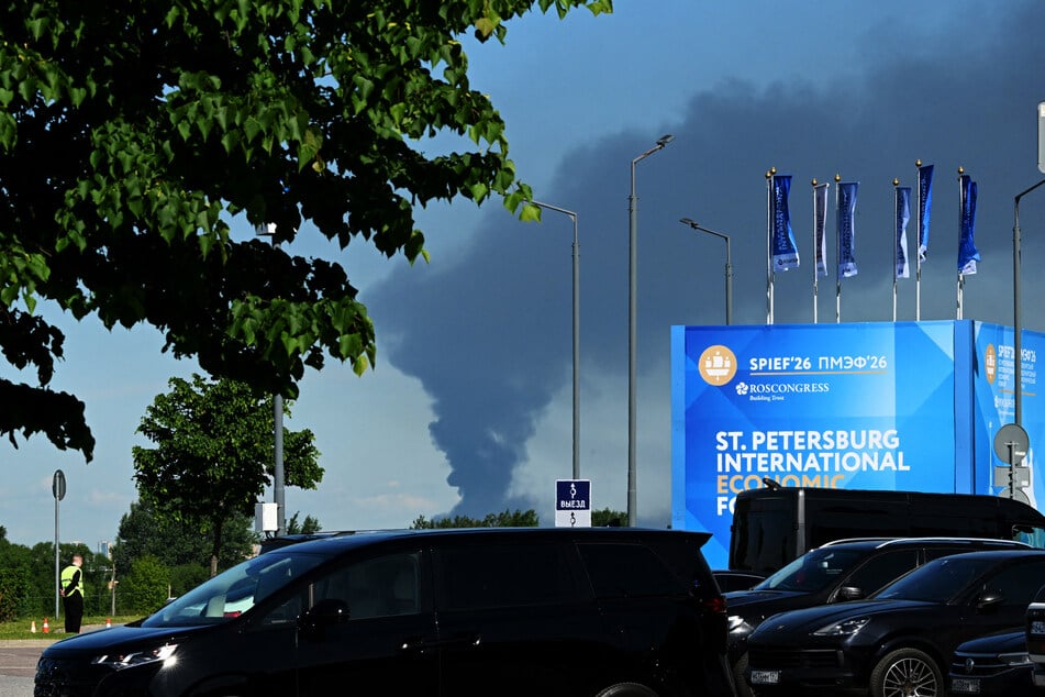Cars are seen parked near banners with branding for the Saint Petersburg International Economic Forum as black smoke rises in distance on June 3, 2026.