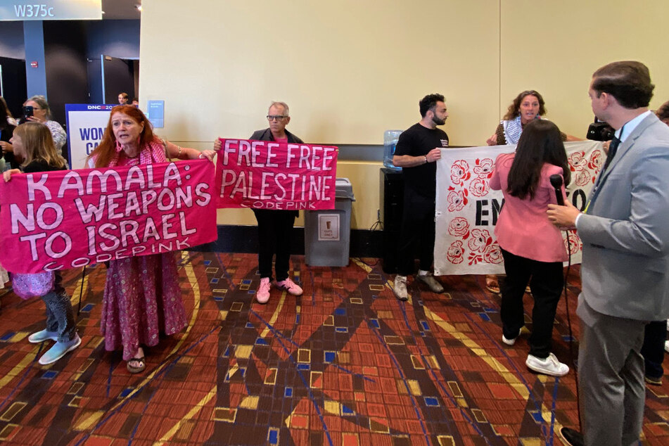 CODEPINK activists raise "Free Free Palestine" and "Kamala: No Weapons to Israel" banners outside the Democratic National Convention's Women's Caucus meeting in Chicago, Illinois.