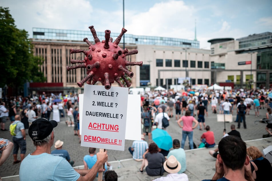 Ein Teilnehmer der Demonstration hält ein Schild mit einem Coronavirus-Symbol in die Höhe.