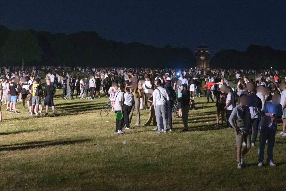 Kleinere und größere Menschengruppen stehen auf der Stadtpark-Wiese im Schein des von der Polizei aufgestellten Lichtmastes.