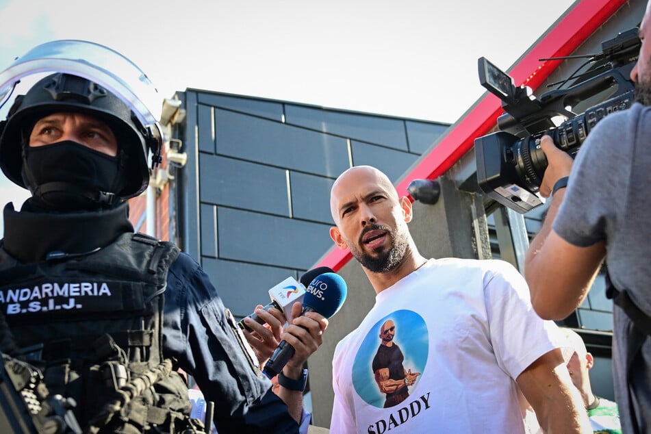 Andrew Tate (c.), speaks to journalists as he is brought in for questioning by the Romanian gendarmes after a 10-hour long raid by police at their residency in Bucharest on August 21, 2024.