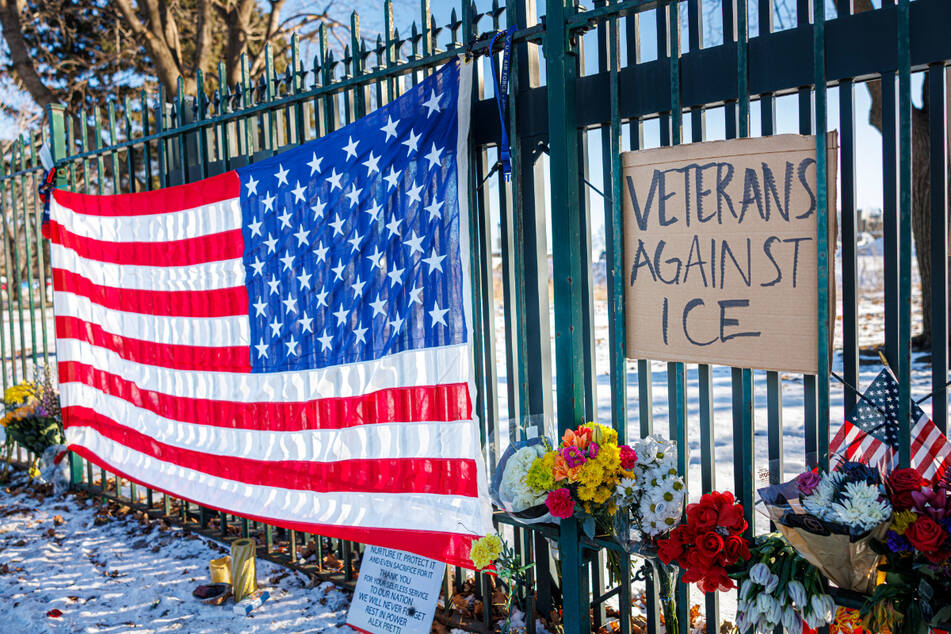 Eine US-Flagge und ein Schild mit der Aufschrift "Veterans Against ICE" hängen neben Blumen an einer Gedenkstätte zu Ehren von Alex Pretti.