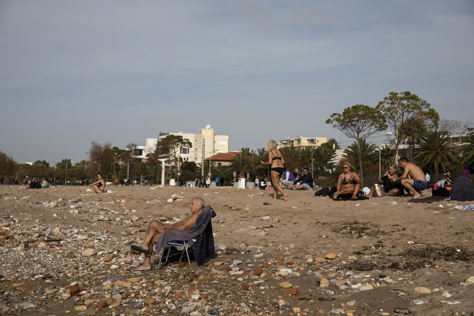 Trotz der geltenden Corona-Beschränkungen sitzen die Menschen am Sonntag an einem Strand im Athener Vorort Glyfada und genießen das warme Wetter.