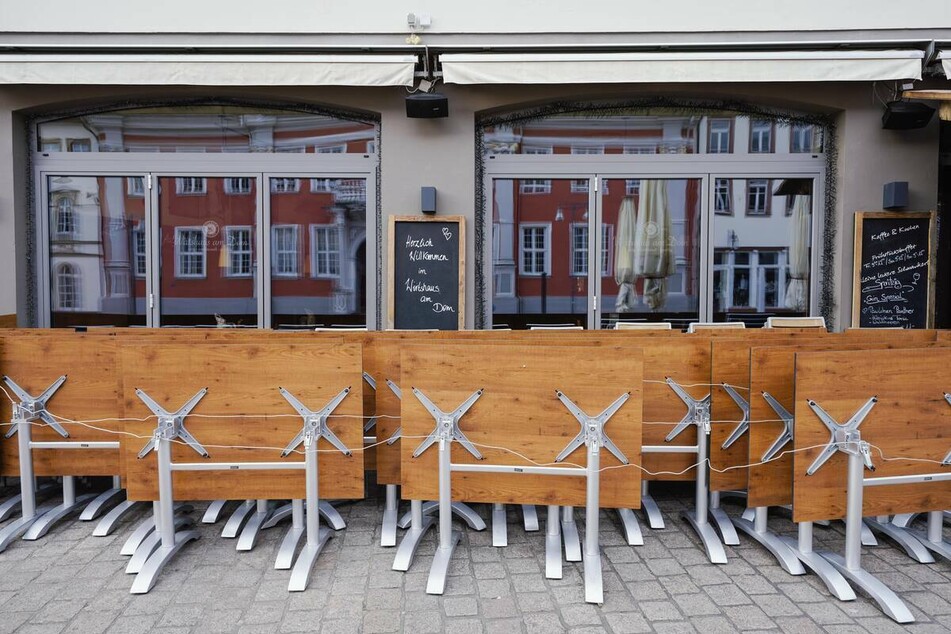 Hochgeklappte Tische stehen in der Fußgängerzone vor einer Gastwirtschaft.