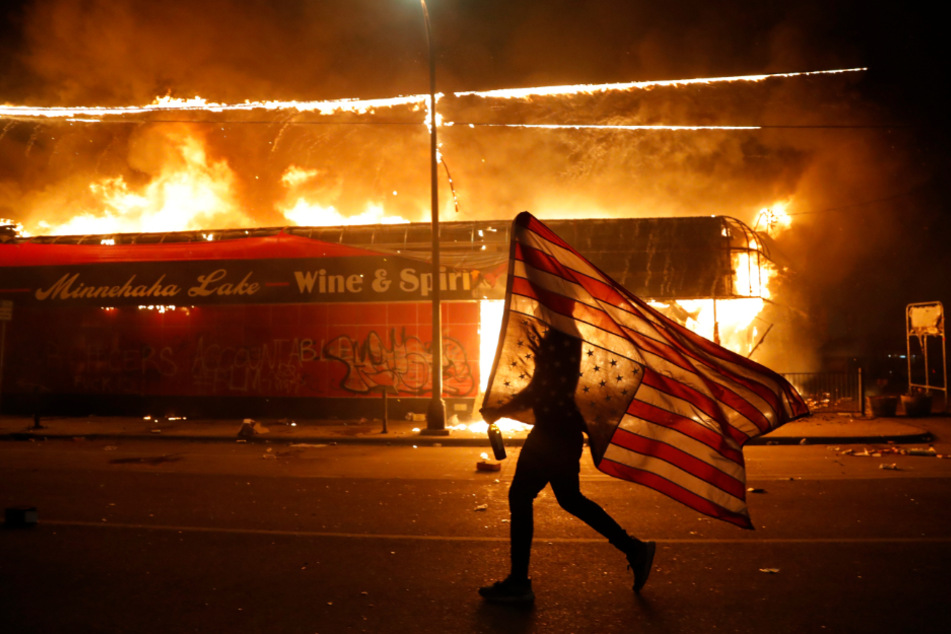 Ein Demonstrant trägt neben einem brennenden Gebäude eine US-Flagge während der Proteste nach dem Tod von George Floyd, der in Folge einer brutalen Festnahme durch einen Polizisten in Minneapolis starb.