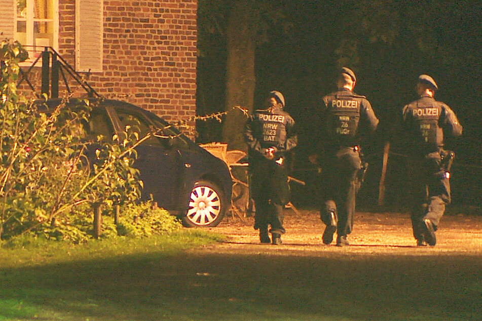 Polizeibeamte gehen zu einem weiteren Haus auf dem großen Grundstück.