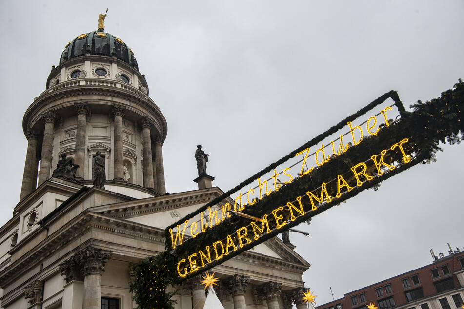 Eine Dekoration mit der Aufschrift "WeihnachtsZauber Gendarmenmarkt" hängt über einem der Eingänge zum Weihnachtsmarkt auf dem Gendarmenmarkt.