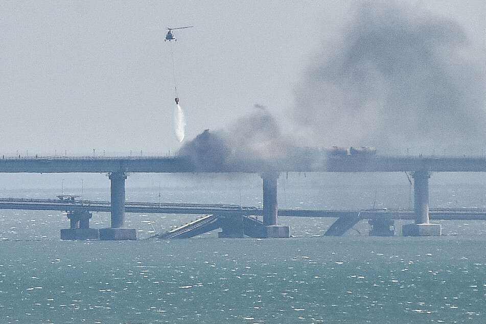 Ein Löschhubschrauber wirft Wasser über dem brennenden Zug auf der Krim-Brücke ab.