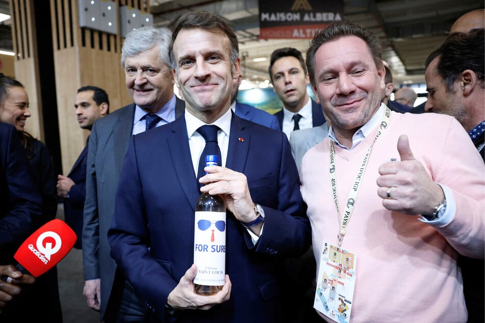 French President Emmanuel Macron (C-R) holds a bottle of "For Sure" wine next as he visits the Wine Paris trade fair Paris, France on February 9, 2026.