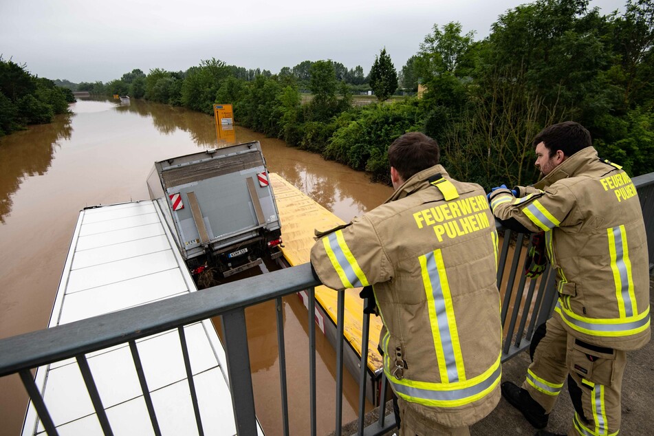 Zwei Feuerwehrleute blicken über die überflutete Bundesstraße 265, die durch Nordrhein-Westfalen und Rheinland-Pfalz führt – die zwei am stärksten betroffenen Bundesländer.