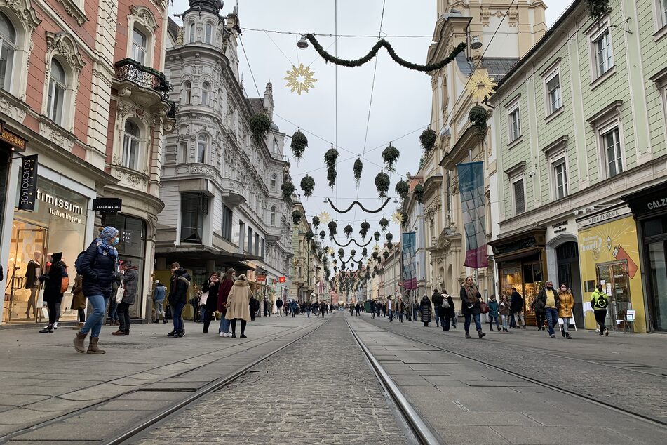Menschen mit Mund-Nasen-Schutz gehen in der Vorweihnachtszeit in der recht leeren Innenstadt an Geschäften vorbei. Österreich geht ab dem 26. Dezember für mindestens drei Wochen erneut in den coronabedingten Lockdown.