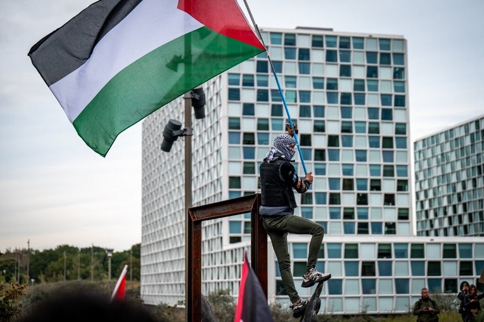 A protestor wearing a keffiyeh waves a Palestinian flag during a Gaza solidarity demonstration in front of the International Criminal Court in the Hague, Netherlands.