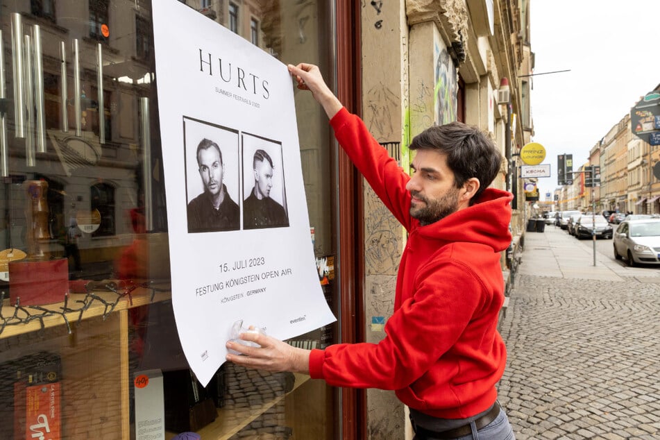 Peter Pfundt klebt an das Schaufenster seines Musikhauses ein Plakat vom "Hurts"-Auftritt auf der Festung Königstein.