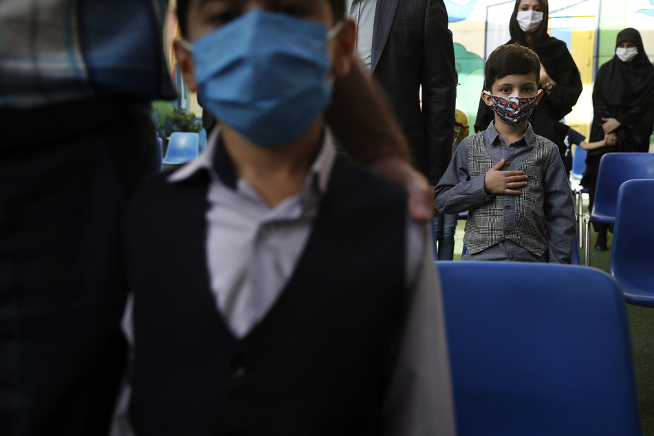 Schüler und ihre Eltern tragen Schutzmasken, um die Verbreitung des Coronavirus zu verhindern und hören die Nationalhymne, während der Eröffnungszeremonie der Hashtroudi-Schule.