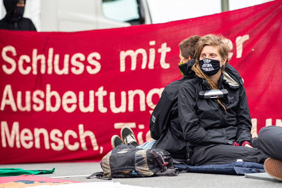 Aktivisten vom "Bündnis Gemeinsam gegen die Tierindustrie" haben die Einfahrt der Firma Tönnies besetzt, zwei davon haben sich mit Fahrradschlössern um den Hals angekettet und sitzen vor den Transparenten.