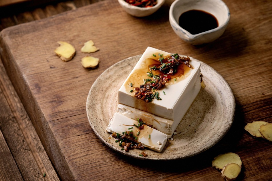 Yum! Silk tofu japanese soy cheese with chili ginger, chive and soy sauce topping on ceramic plate over wooden table.