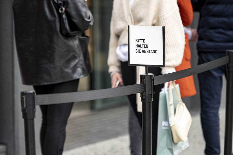 Neben einer Schlange vor einem Geschäft am Ku'Damm steht ein Hinweisschild mit der Aufschrift "Bitte halten Sie Abstand". Aufgrund der Corona-Pandemie wird ein negativer Corona-Test zum Einkaufen in Geschäften, für Besuche im Friseur- oder Kosmetiksalon, in Museen und Galerien benötigt.