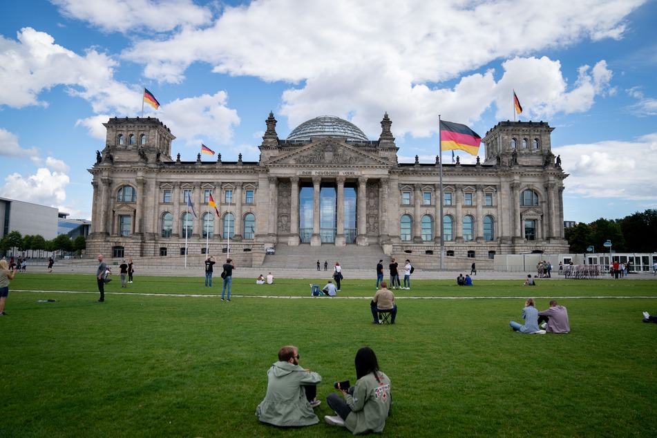 Passanten sitzen auf der Wiese vor dem Reichstagsgebäude.