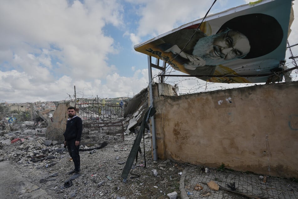 in Mann steht neben einem Plakat, das den getöteten Hisbollah-Führer Nasrallah zeigt, an der Stelle eines zerstörten Hauses, das bei einem israelischen Luftangriff im Dorf Sarafand im Südlibanon getroffen wurde.