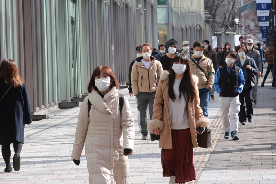 Passanten tragen Schutzmasken und gehen einen Bürgersteig in Tokio entlang.