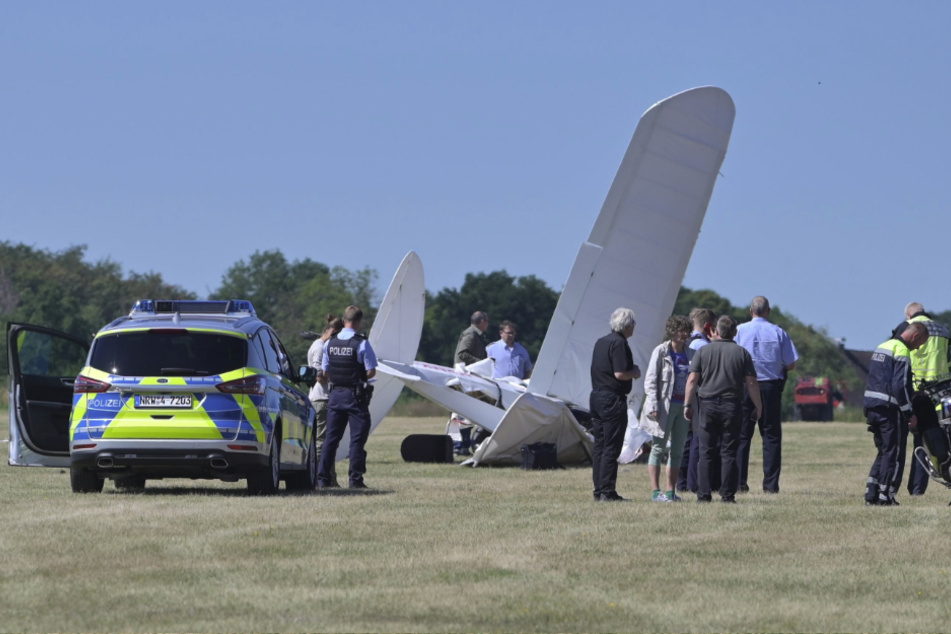 Feuerwehr, Polizei und Rettungsdienst-Mitarbeiter stehen am Flughafen Iserlohn-Rheinermark an der Stelle, an der ein Leichtflugzeug abgestürzt ist.
