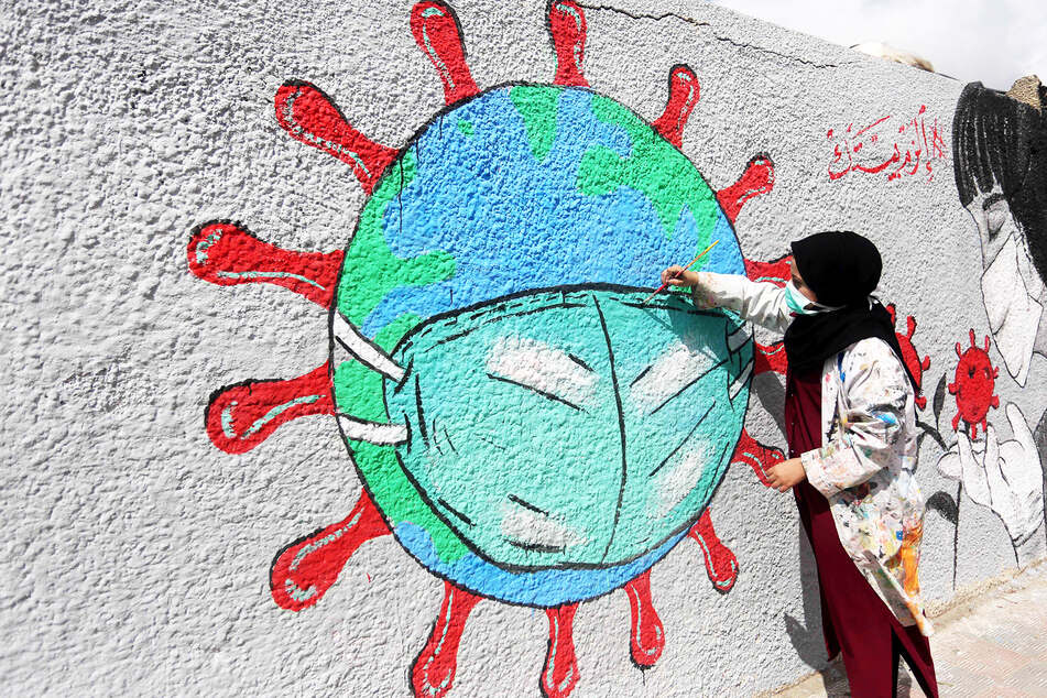 Eine Frau malt eine Erdkugel im Coronavirus-Stil mit Mundschutzmaske an eine Wand (Archivbild).