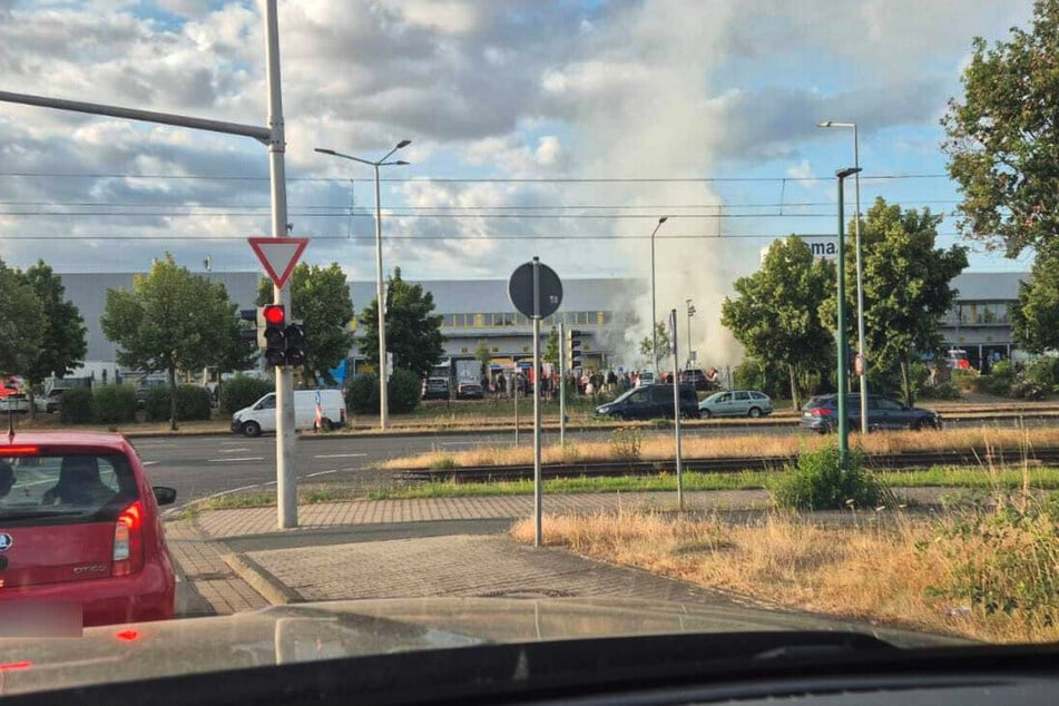 Mehrere Menschen stehen auf dem Firmengelände, während im Hintergrund Rauch aufsteigt.
