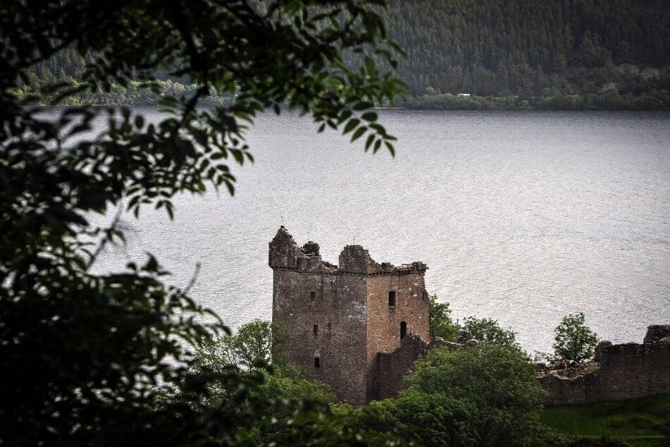 Urquhart Castle is seen through trees beside Loch Ness in Drumnadrochit, Scotland.