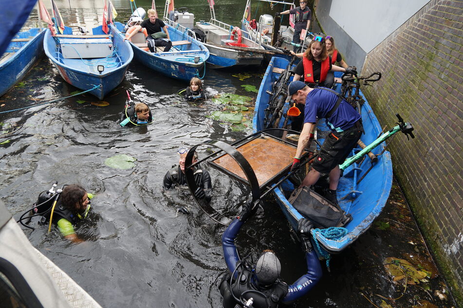 Die von den Tauchern gefundenen Gegenstände wurden von weiteren Helfern in die Boote gehoben. Hier wird gerade ein Werbeschild von Reporter Frank Bründel (m.) und FSJler Paul aus dem Wasser gehievt. Auch TAG24-Reporterin Madita (l.) beteiligte sich an der Suche.