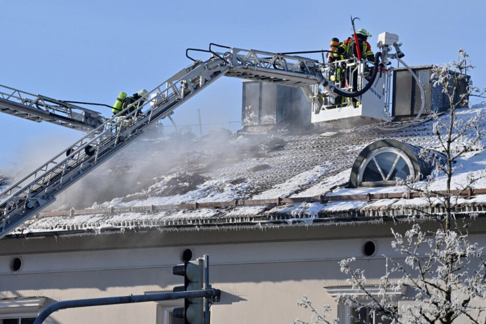 Feuerwehrleute auf Drehstühlen suchen im Dachstuhl des Rathauses von Sauerlach nach Glutnestern.