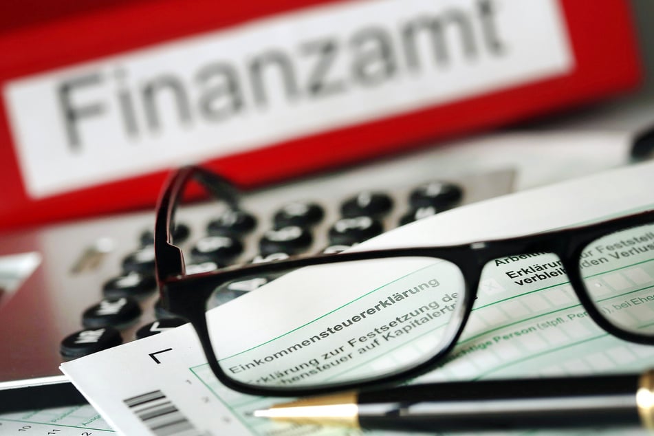 Auf einem Vordruck für die Steuererklärung liegt vor dem Aktenordner mit dem Aufdruck «Finanzamt» ein Stift und eine Brille.