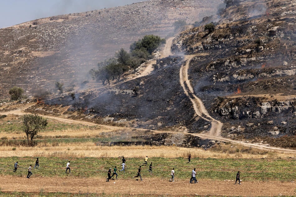 Palestinians run across a field as they try to chase off Israeli settlers on hilltop in the village of Sinjil, in the occupied West Bank on July 4, 2025.