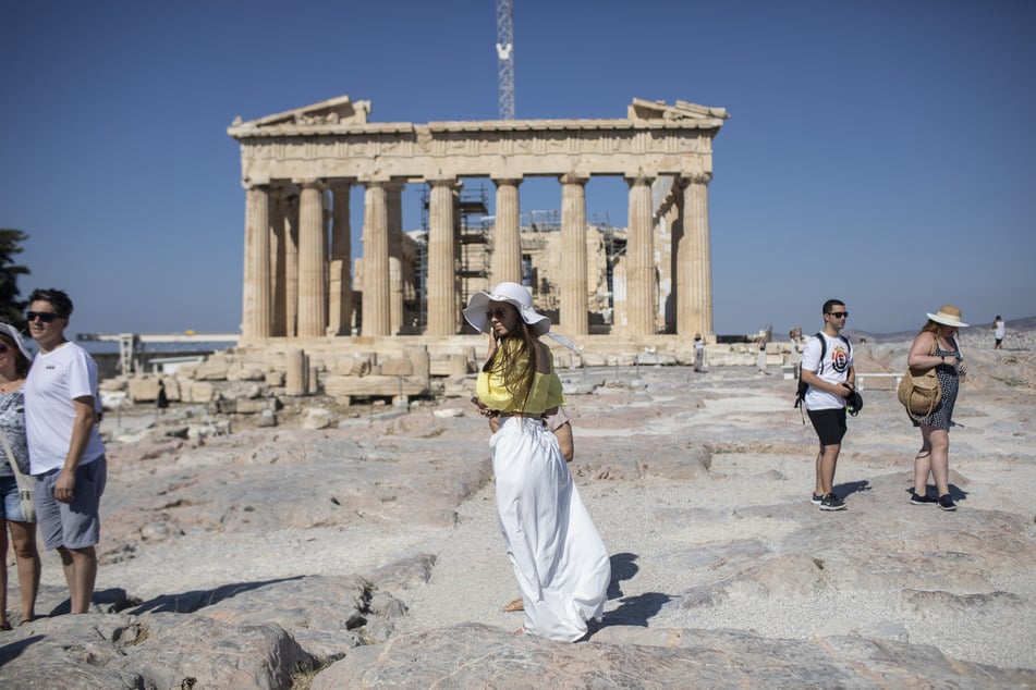 Touristen spazieren über die Athener Akropolis und machen Fotos vor dem Parthenon.