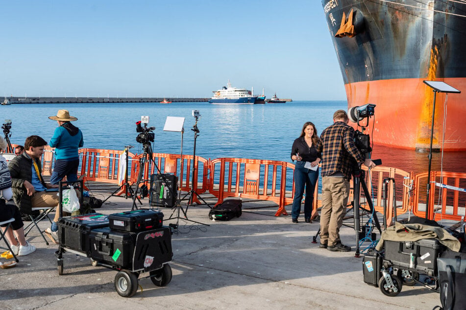 Das Kreuzfahrtschiff "MV Hondius" liegt im Hafen von Granadilla vor Anker. Es ist im Hintergrund zu erkennen, während Reporter aus der Gegend über das dort festgestellte Hantavirus berichten.