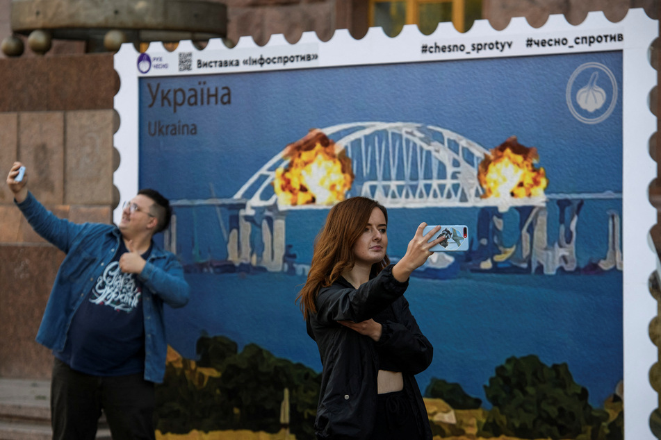 People in Kyiv take photos with artwork depicting the Kerch bridge to Crimea blowing up.