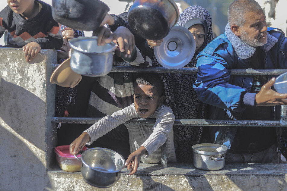 Palästinenser versammeln sich mit Töpfen an einer Spendenstelle, um Lebensmittel entgegenzunehmen.