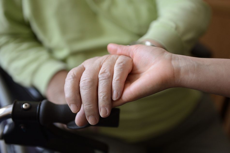 Eine junge Frau hält in einem Seniorenpflegeheim die Hände eines alten Mannes.
