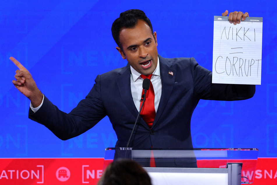 Republican presidential candidate and businessman Vivek Ramaswamy holds up a handwritten sign referring to Nikki Haley as "corrupt."