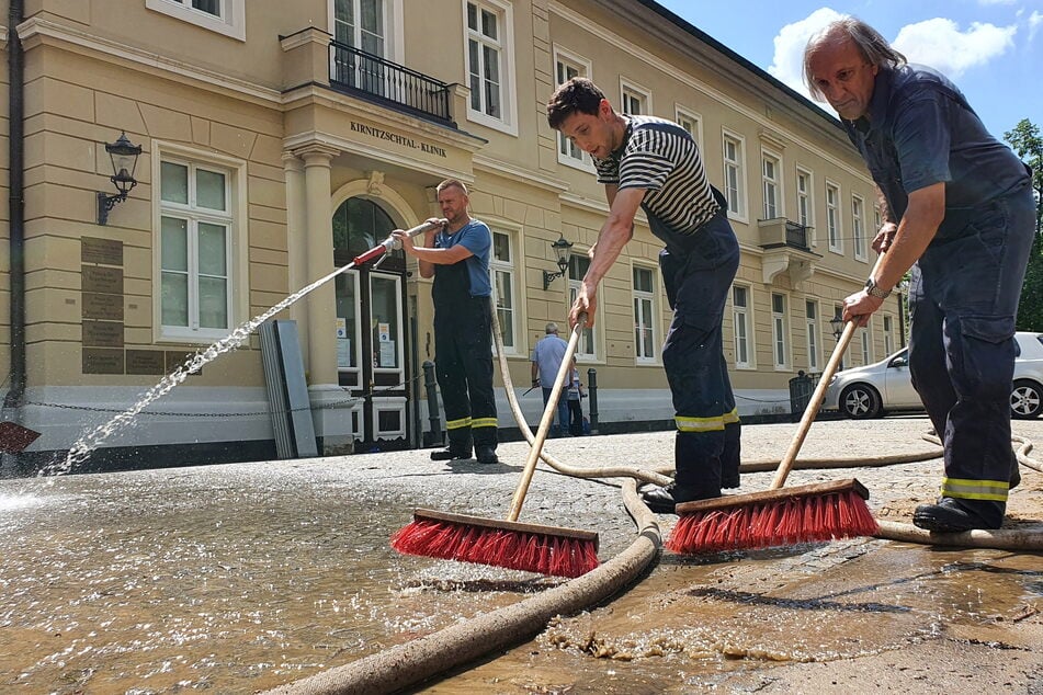 Feuerwehrleute beseitigen vor der Kirnitzschtal-Klinik Bad Schandau Schlamm und Dreck.