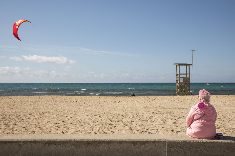 Eine deutsche Touristin sieht ihrem Sohn beim Kitesurfen an einem stürmischen Tag an der Promenade Playa de Palma zu.