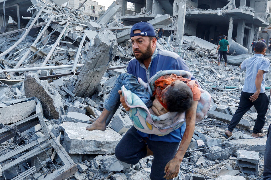 A Palestinian man carries an injured child away from the rubble of a building in the aftermath of an Israeli airstrike.