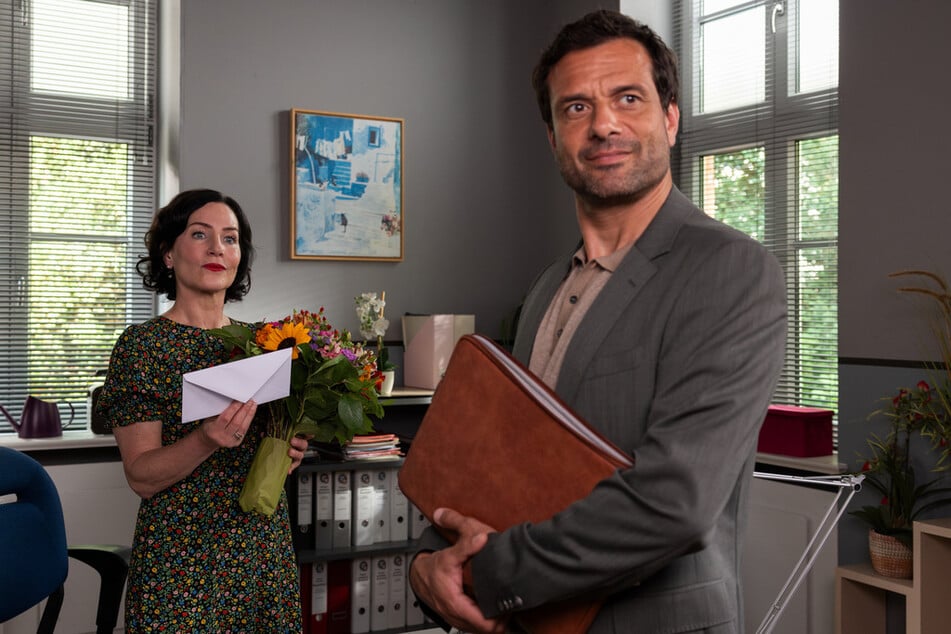 Bevor der Headhunter Thomas Ritter (Kai Schumann, r.) wieder abreisen muss, übergibt er Miriam Stockl (Marisa Burger, l.) einen Strauß Blumen sowie einen Umschlag in beruflicher Sache.