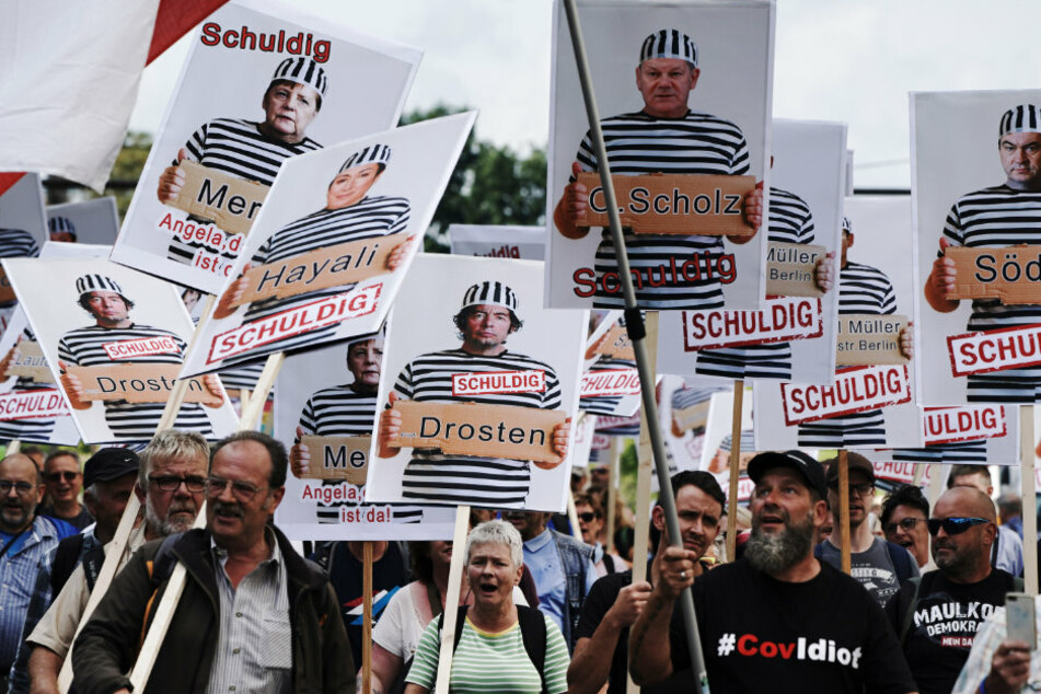 Teilnehmer einer Demonstration gegen die Corona-Maßnahmen halten Schilder mit Fotos von Politikern, Journalisten und Wissenschaftlern jeweils mit Namen und "Schuldig".