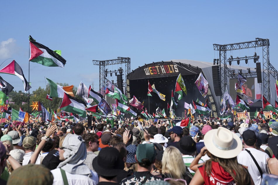 Festivalbesucher sehen den Auftritt des Hip-Hop-Trios Kneecap. Palästina- und Irland-Flaggen wehen im Publikum.