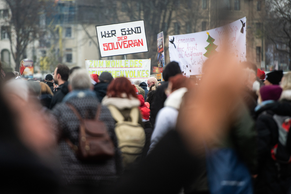 Demonstranten halten bei einer Demonstration am Rheinufer ein Schild mit der Aufschrift "Wir sind der souverän" in die Höhe.