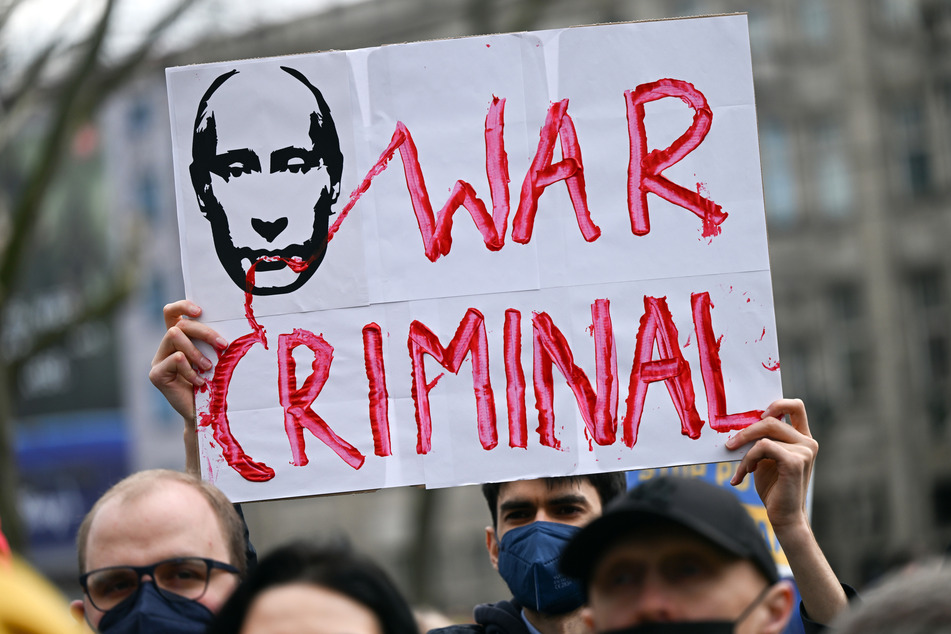 Ein Demonstrant hält bei einer Demonstration in Köln ein Plakat mit dem Konterfei des russischen Präsidenten Putin und der Aufschrift "War Criminal" in den Händen.